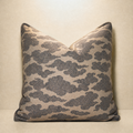 A square decorative throw pillow with a beige background and a dark gray cloud pattern, set against a matching beige backdrop.