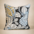 A square decorative throw pillow featuring an intricate woven floral and paisley pattern in light blue, beige, gray, and black, set against a solid beige background.